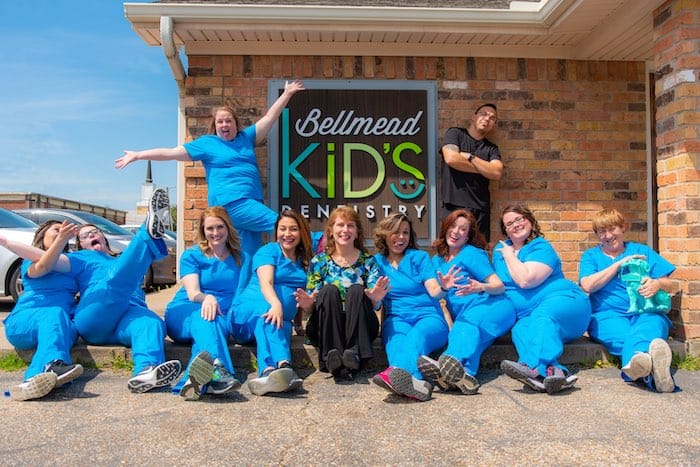 Bellmead Kids Dentistry Dr. Susan Francis with all the office team members wearing blue uniform standing for a photo shoot outside the office in front of the office name on the brick wall