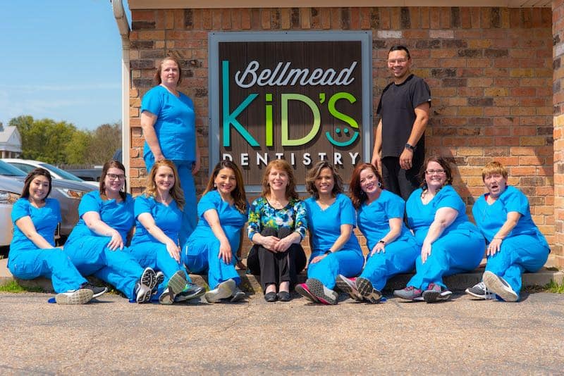 Children's dentist in Waco, TX Dental team smiling while sitting in front of office sign