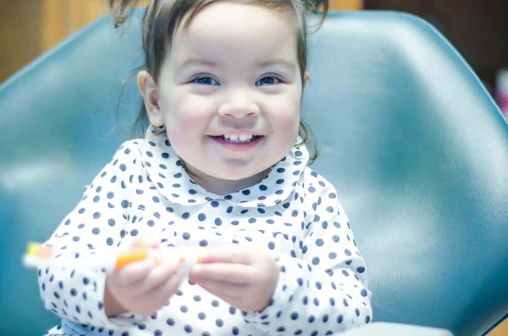 Bellmead Kids Dentistry 3 year old pediatric patient smiling while sitting in the dentist chair holding a tooth brush